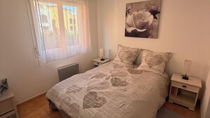 Een slaapkamer met een groot bed, een nachtkastje, een raam met gordijnen en een aan de muur hangend schilderij.