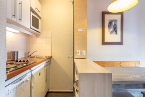 A compact kitchen with a microwave, stove, and sink. There is a wooden bench and a framed picture on the wall. - Alpine 1-Bed Apartment in Tignes (Tignes)