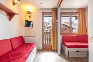 A room with a red sofa, a television mounted on the wall, and a window with curtains. - Alpine Ski Apartment in Tignes for 4 (Tignes)