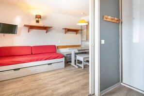 A room with a red sofa, a small table, and a TV mounted on the wall. - Alpine Stay with Private Balcony (Tignes)