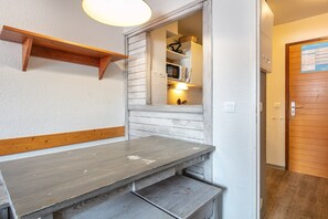 A small kitchenette with a microwave, a shelf, and a wooden bench. - Alpine Stay with Private Balcony (Tignes)