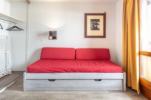 A single bed with a red mattress and wooden frame, a wall-mounted light, a framed picture, and a window with curtains. - Alpine Stay with Private Balcony (Tignes)