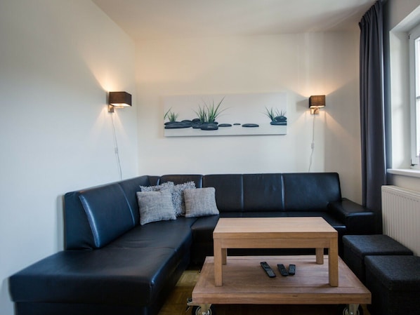Una sala de estar moderna con un sofá de cuero negro, una mesa de centro de madera y dos lámparas de pared.