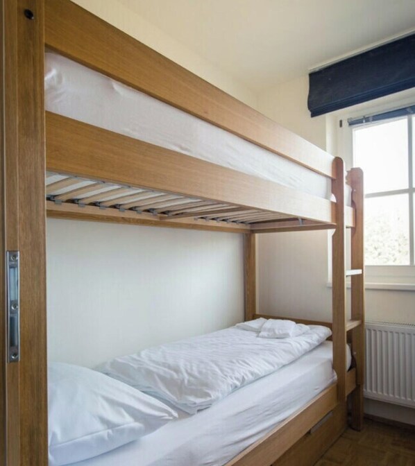 Uma cama beliche com estrutura de madeira, roupa de cama branca e janela com vista.