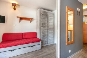 A room with a red sofa, a wooden shelf, a wardrobe, and a mirror on the wall. - Tignes Stay near Lifts (Tignes)