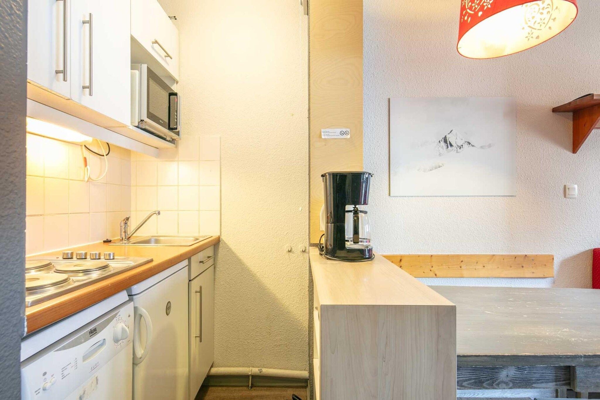 Una cocina funcional con estufa, microondas y lavaplatos. Hay una cafetera sobre la encimera y un cuadro en la pared.
