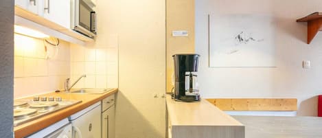 Una cocina funcional con estufa, microondas y lavaplatos. Hay una cafetera sobre la encimera y un cuadro en la pared.