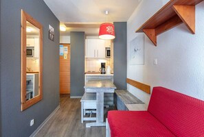 A compact kitchen with a dining area, a red sofa, and a wooden ceiling beam. - Tignes Stay near Lifts (Tignes)