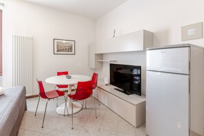 A compact kitchen with a white refrigerator, a flat-screen TV, and a dining table with red chairs. - Le Charme, heart of Verona (Verona)