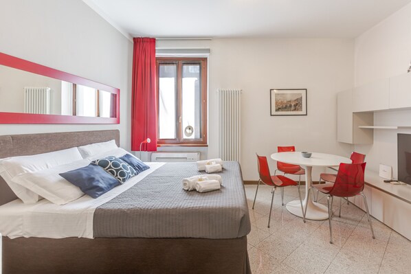A hotel room with a bed, a dining table with chairs, a window with curtains, a radiator, and a painting on the wall. - Le Charme, heart of Verona (Verona)