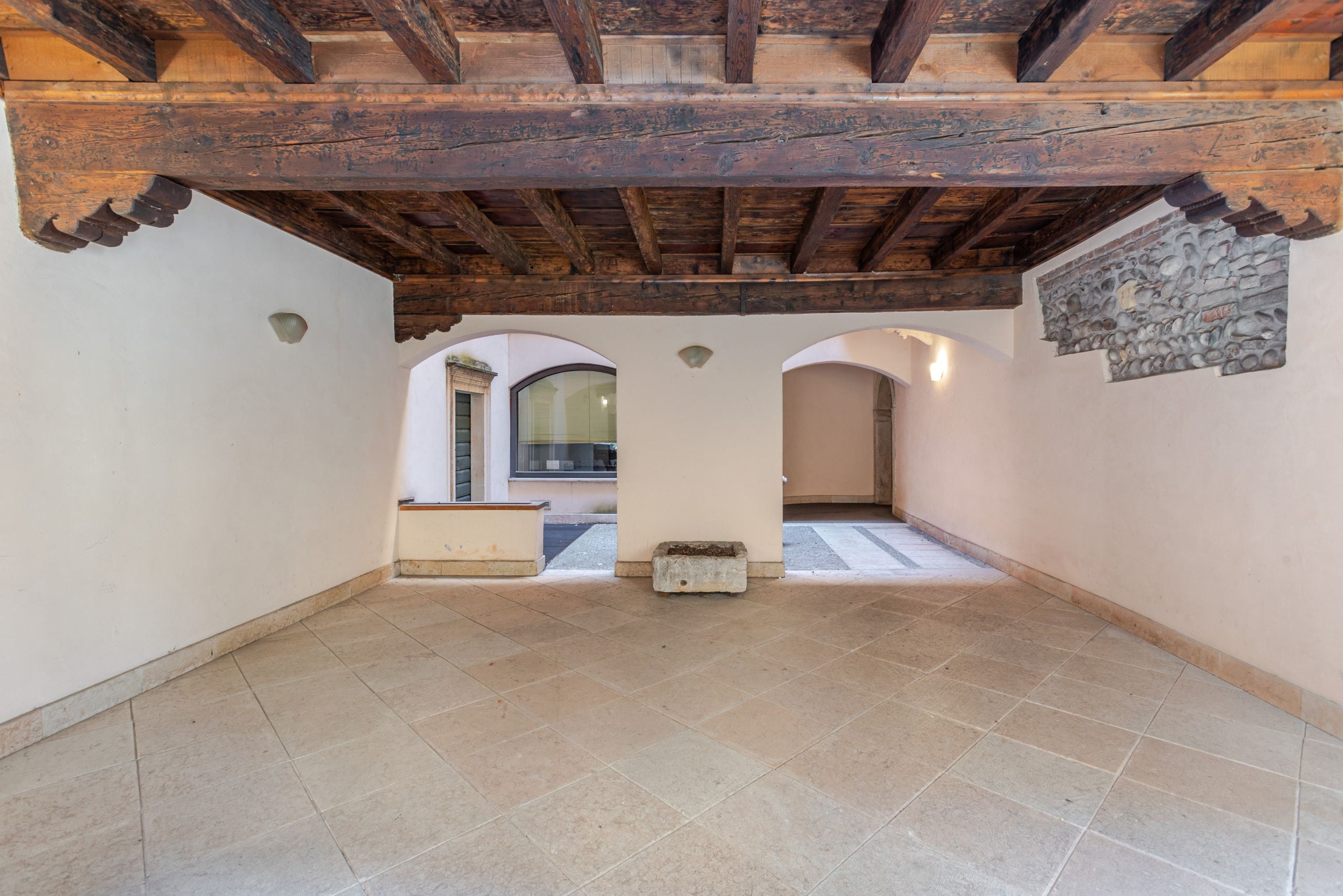 A spacious attic room with a sloped ceiling, stone wall decoration, and a view through an arched doorway.