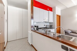 A modern kitchen with white cabinets, a red accent wall, a stainless steel sink, and a built-in stove. - Le Charme, heart of Verona (Verona)
