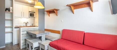 Ein kompakter Wohnbereich mit Küchenzeile, einem Essbereich mit Tisch und Bänken sowie einem roten Sofa.