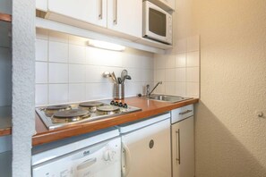 Une cuisine compacte avec des meubles blancs, un four à micro-ondes, un évier et un lave-vaisselle.