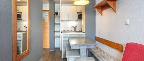A compact kitchen with a dining area, a red sofa, and a wooden shelf.