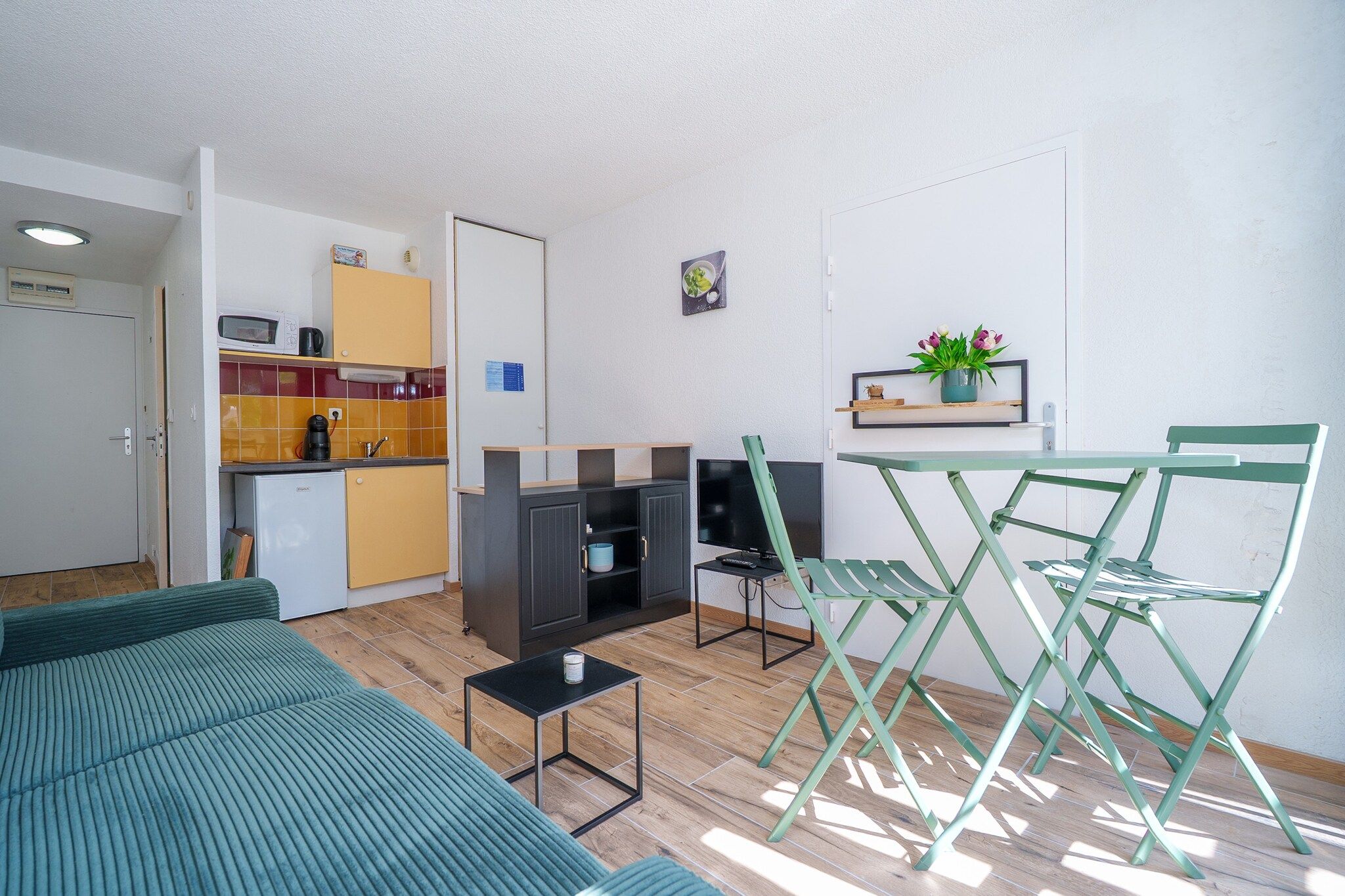 A compact living space with a kitchenette, a sofa, a dining area with chairs, and a TV.