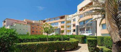 A multi-story residential building with balconies, a paved pathway, and well-maintained greenery.