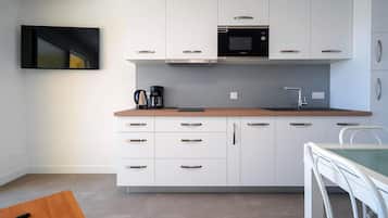 A compact kitchen with white cabinets, a microwave, a coffee maker, and a dining area with a white table and chair.