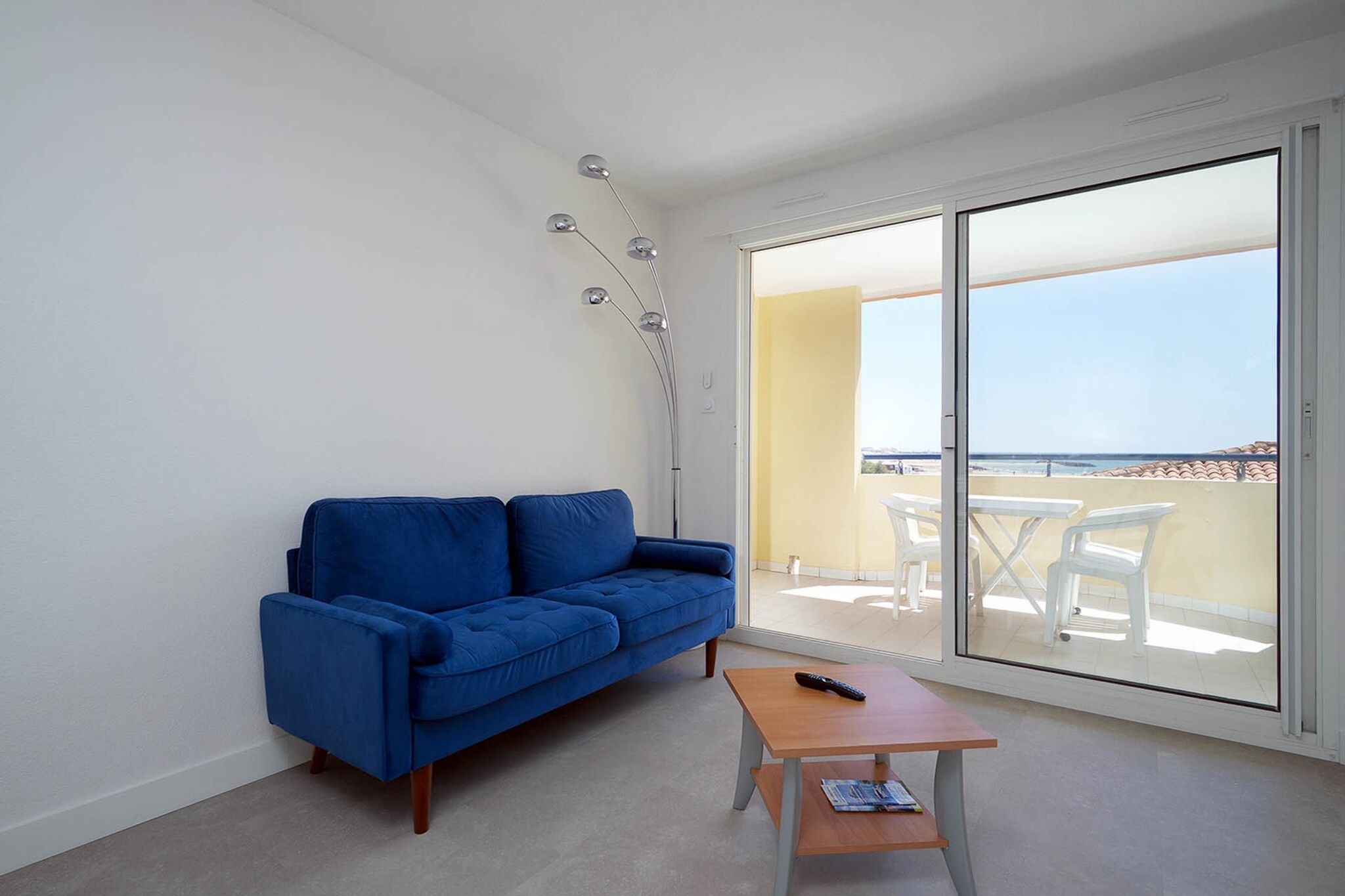 A room with a blue sofa, a small wooden table, and a glass door leading to an outdoor area with a table and chairs.
