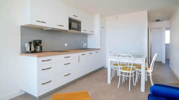 A modern kitchen with white cabinets, a microwave, and a coffee maker. There is a dining area with a table and chairs. A blue sofa is visible in the foreground.