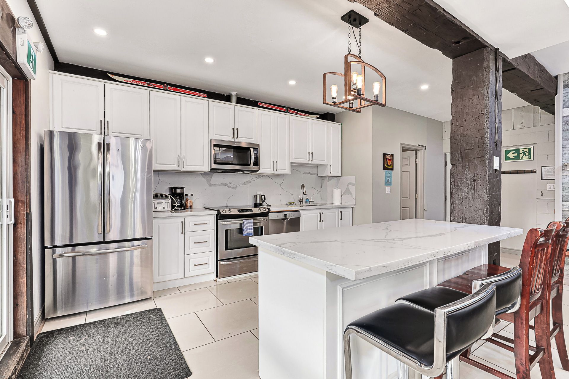 A modern kitchen with white cabinets, stainless steel appliances, a marble countertop, and a central island with bar stools.