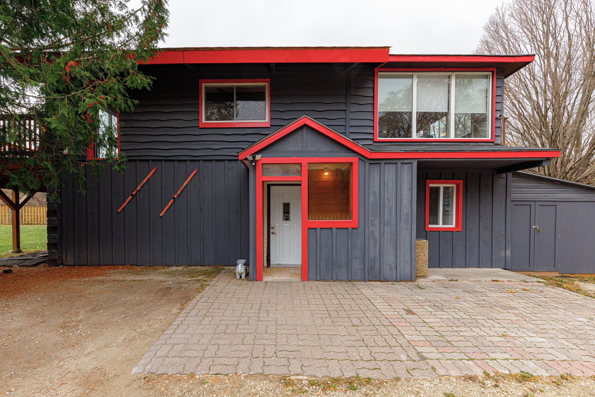 Ein zweistöckiges Haus mit dunkler Fassade und roten Akzenten, mit einer Haustür, zwei Fenstern und einer Garage.
