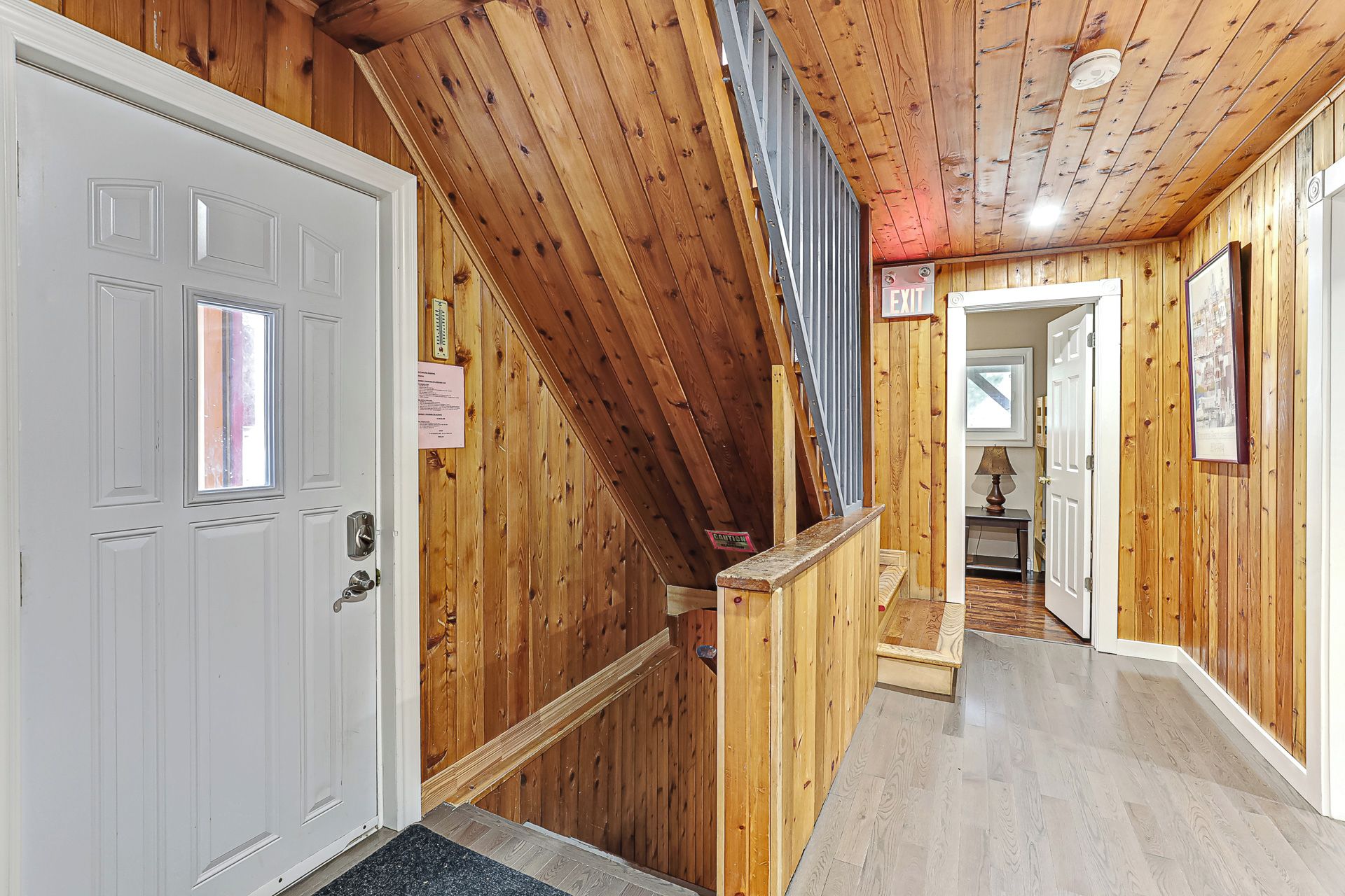 A wooden interior with a white door, a staircase, and a hallway leading to another room.
