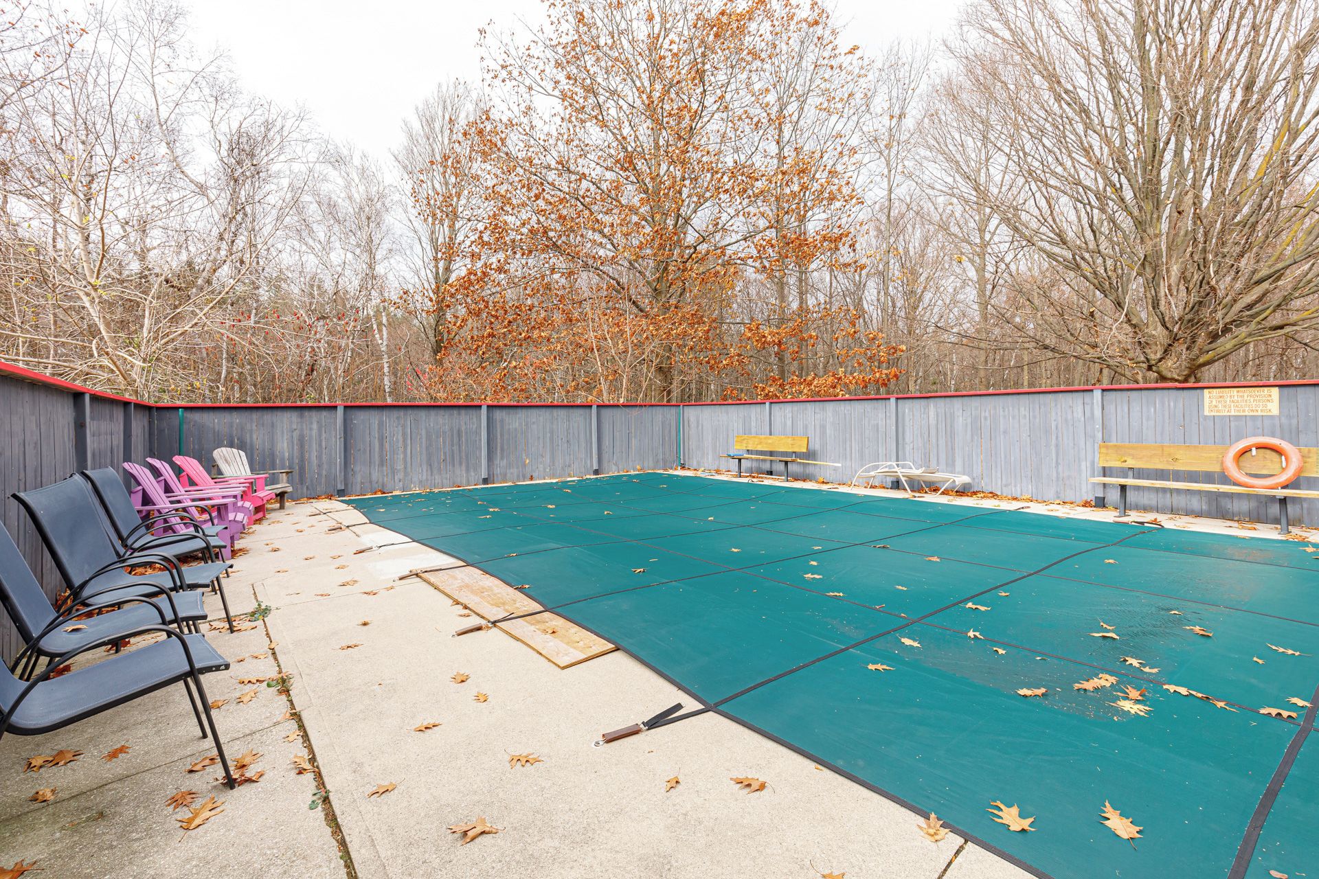 A swimming pool area with a wooden fence, several lounge chairs, and a bench.