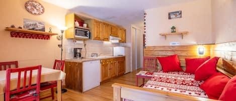 A compact living space with a kitchenette, a dining area, and a bed with red bedding.