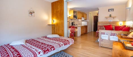 A cozy room with a bed, a wooden desk, a kitchen area, and a dining table.