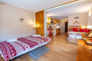 Um quarto aconchegante com uma cama, uma escrivaninha de madeira, uma cozinha e uma mesa de jantar.