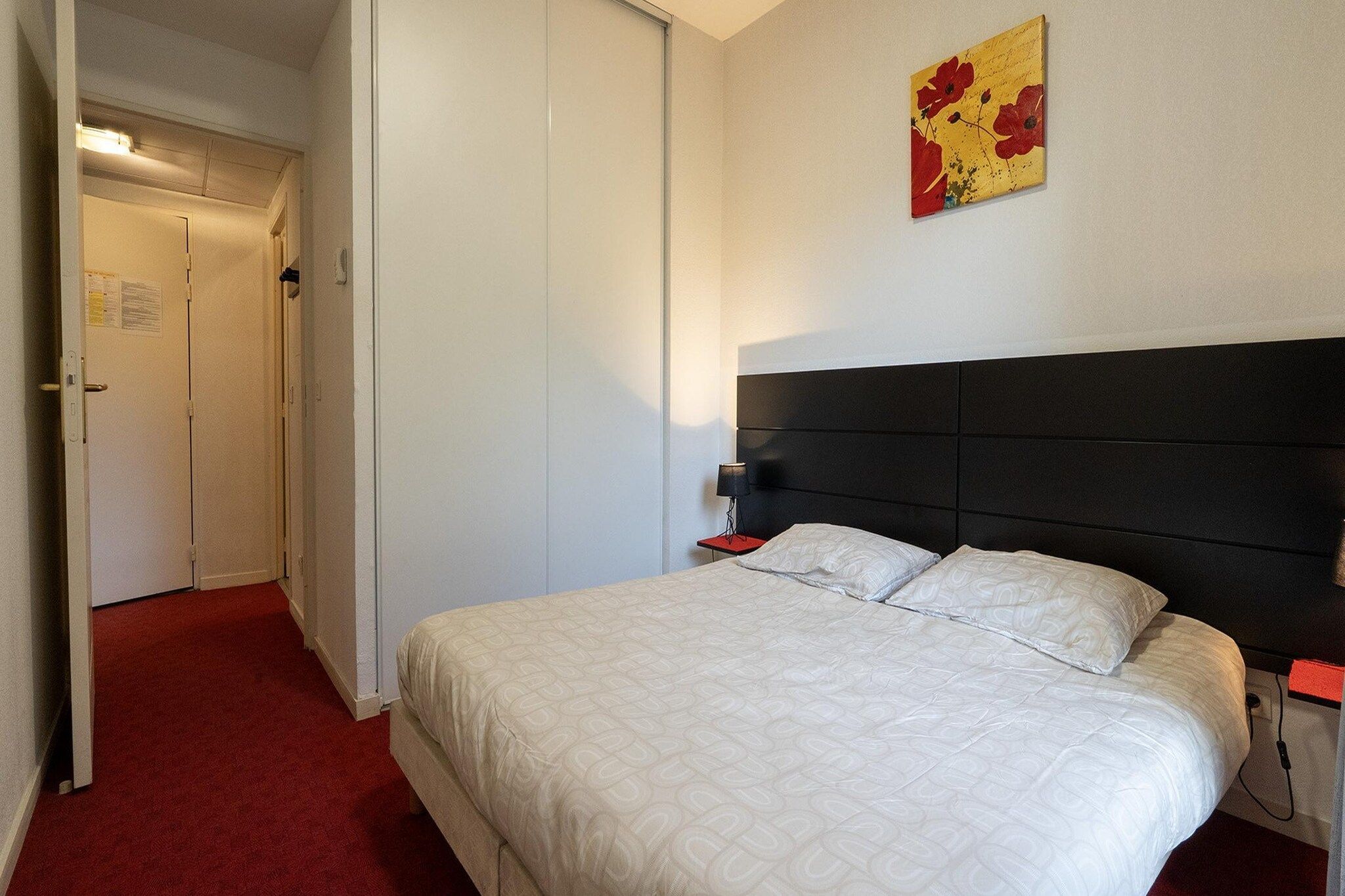 Une chambre d’hôtel avec un lit, une table de chevet, une lampe et une porte.
