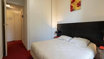 Une chambre d’hôtel avec un lit, une table de chevet, une lampe et une porte.