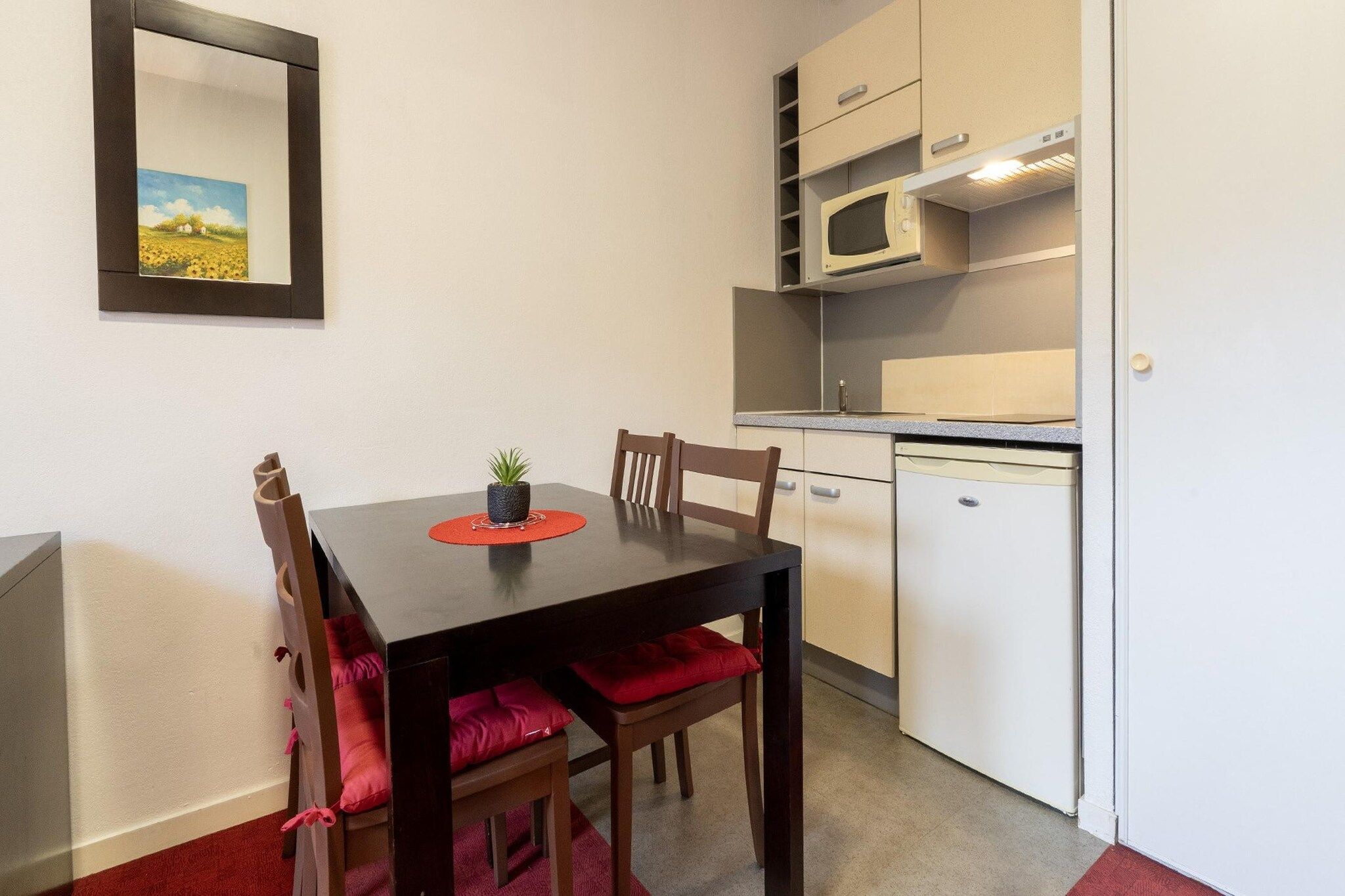 A compact kitchen with a microwave, a small refrigerator, and a dining table with chairs.