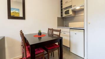 A compact kitchen with a microwave, a small refrigerator, and a dining table with chairs.