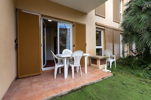 Une terrasse avec une table et des chaises, une porte coulissante et un petit jardin.