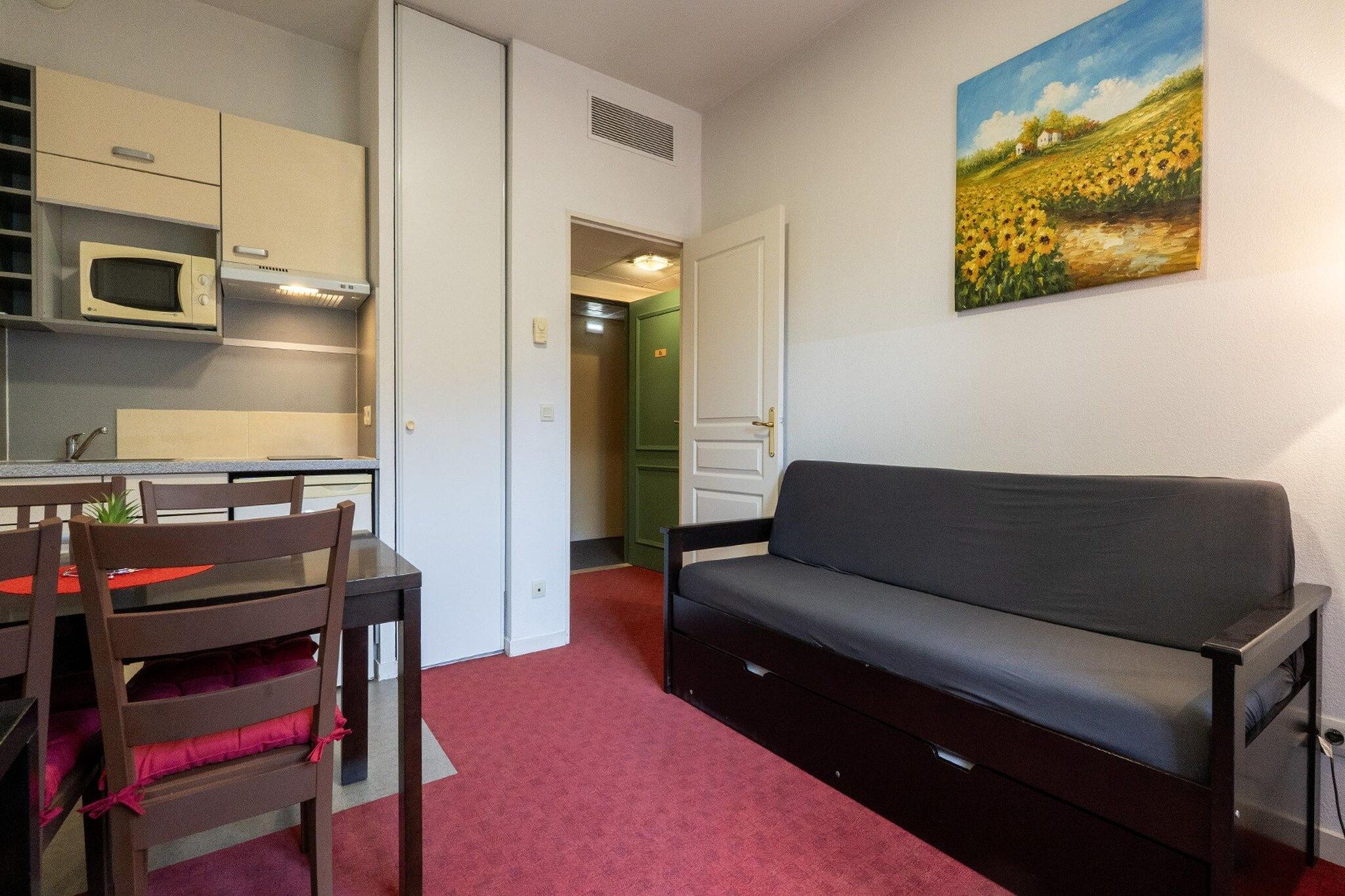 Un espace de vie compact comprenant un coin cuisine, un canapé et un tableau accroché au mur.