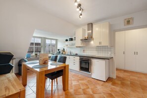 A modern kitchen with white cabinets, a built-in oven, and a dining area with a wooden table and chairs. - Idyllic, Quiet Apartment with Wi-Fi (Grebin)