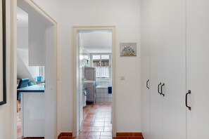 A hallway leading to a kitchen area with a dining table and chairs, a white cabinet, and a window with curtains.
