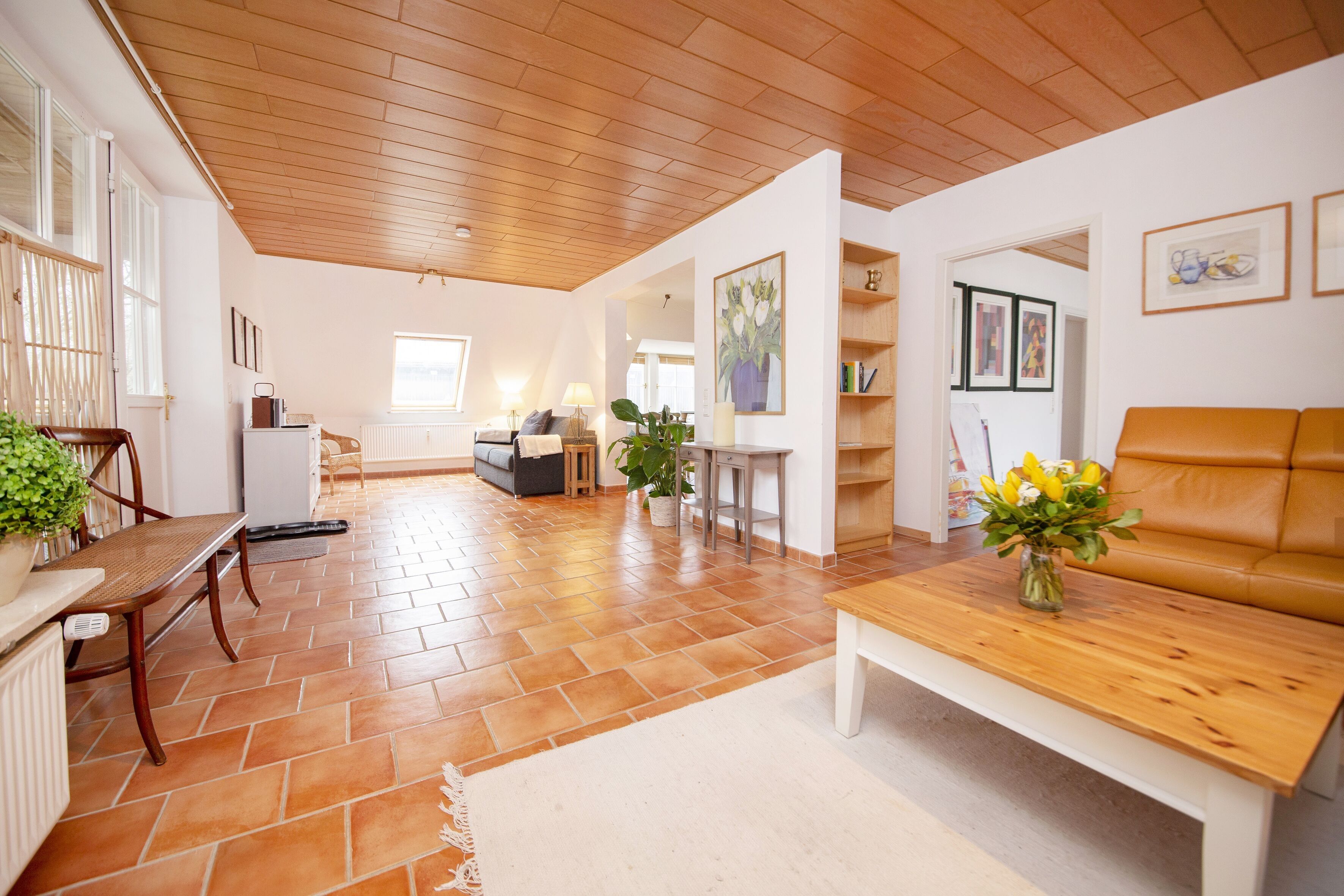 A spacious living area with a wooden ceiling, a sofa, a coffee table, and a dining table with chairs.