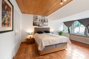 A bedroom with a wooden ceiling, a bed with a grey headboard, a nightstand with a lamp, and a window with curtains. - Idyllic, Quiet Apartment with Wi-Fi (Grebin)