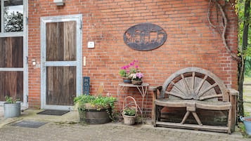 Una pared de ladrillo rústico con un letrero de metal, una puerta de madera, un banco y plantas en macetas.