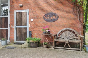A rustic brick wall with a metal sign, a wooden door, a bench, and potted plants.