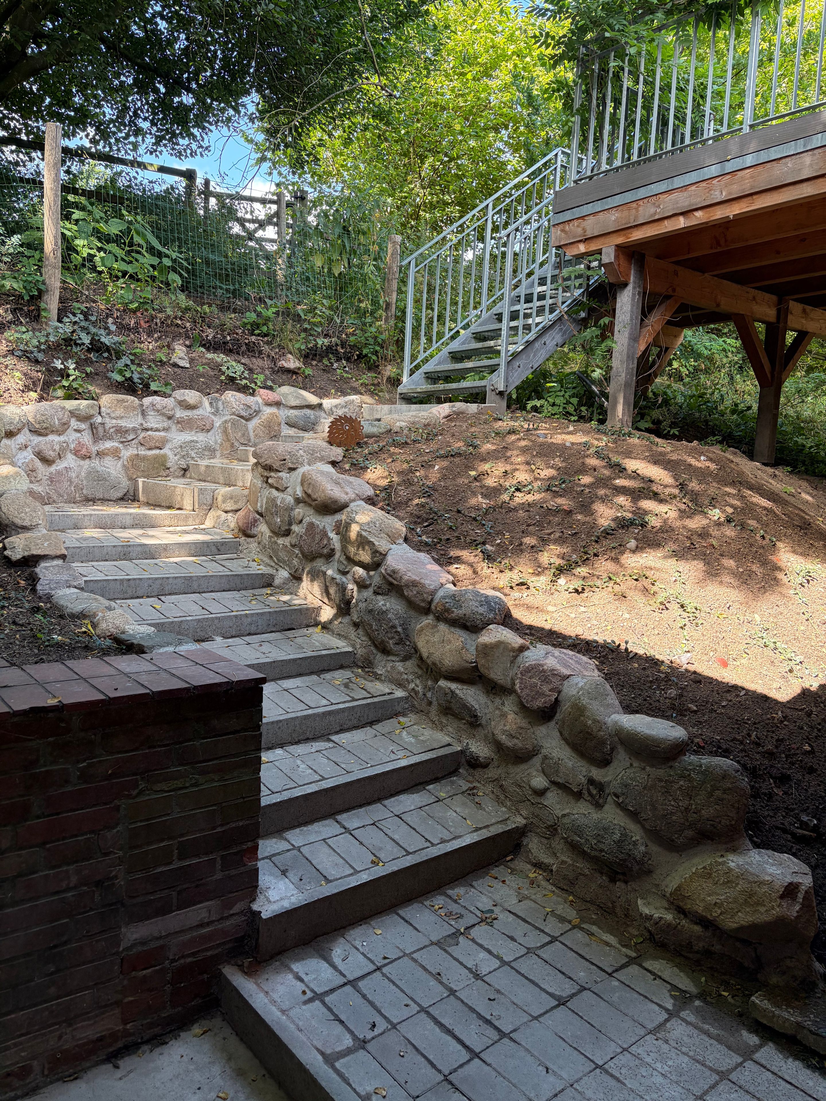 A stone staircase leading up a hill, surrounded by greenery and a metal fence.