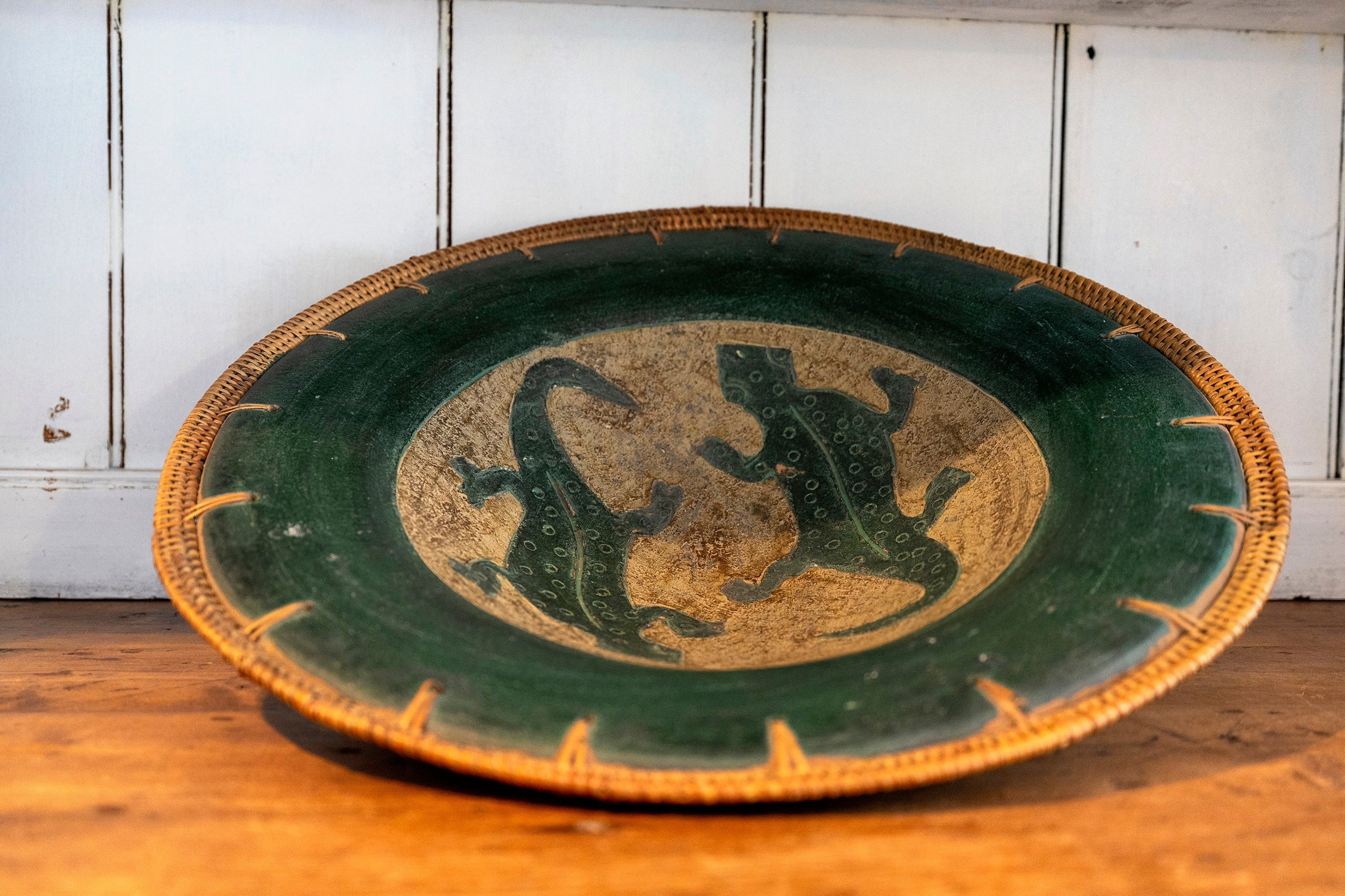 Un plato redondo de cerámica verde y beige con un diseño central en relieve, sobre una superficie de madera sobre fondo blanco.