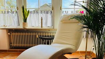Een ligbed met uitzicht op een huis door een raam, een radiator en een potplant.