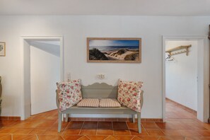 A room with a bench, a painting of a beach, and a wooden coat rack.