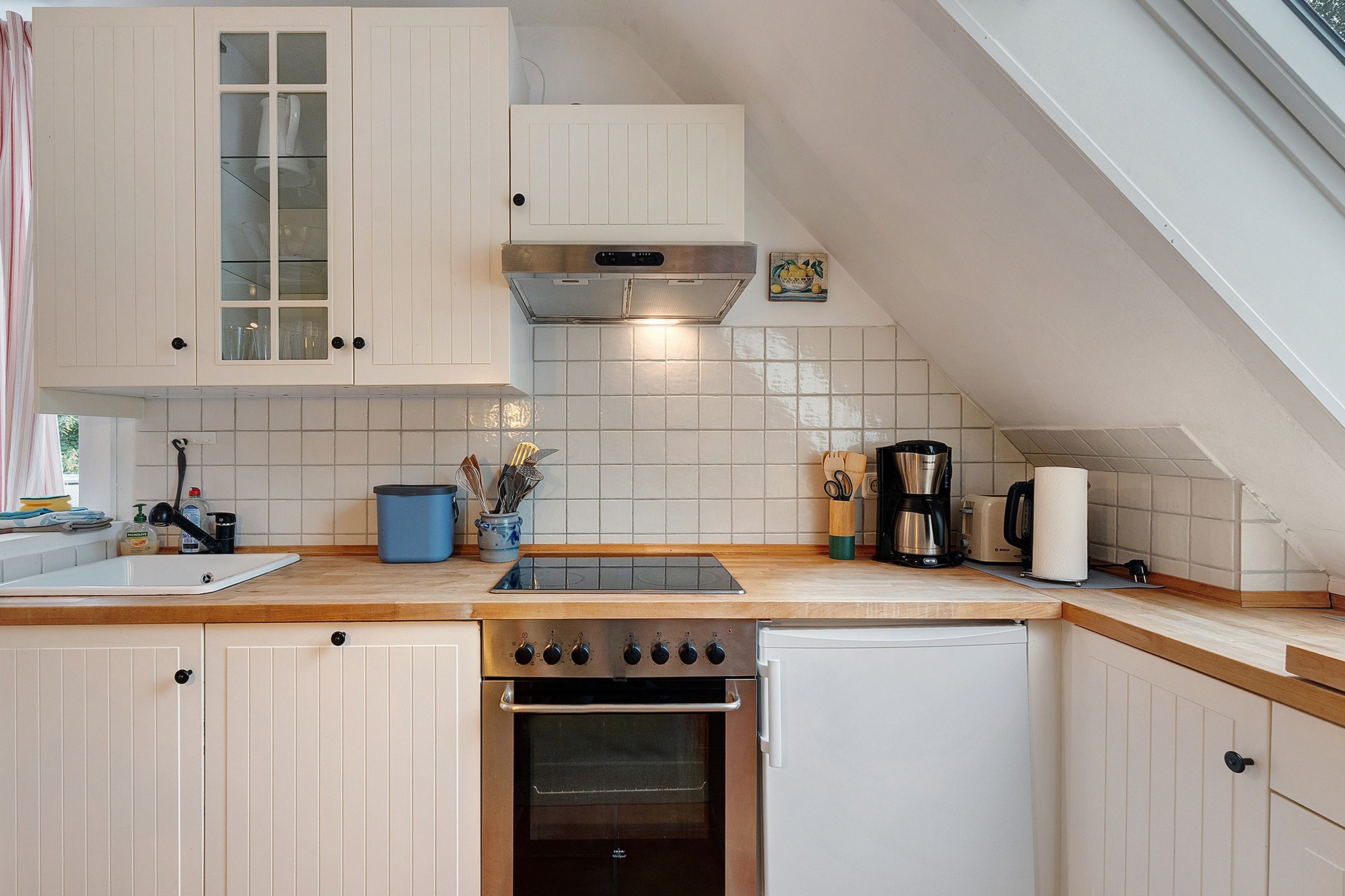 A kitchen with white cabinets, a stove, a sink, and a coffee maker.