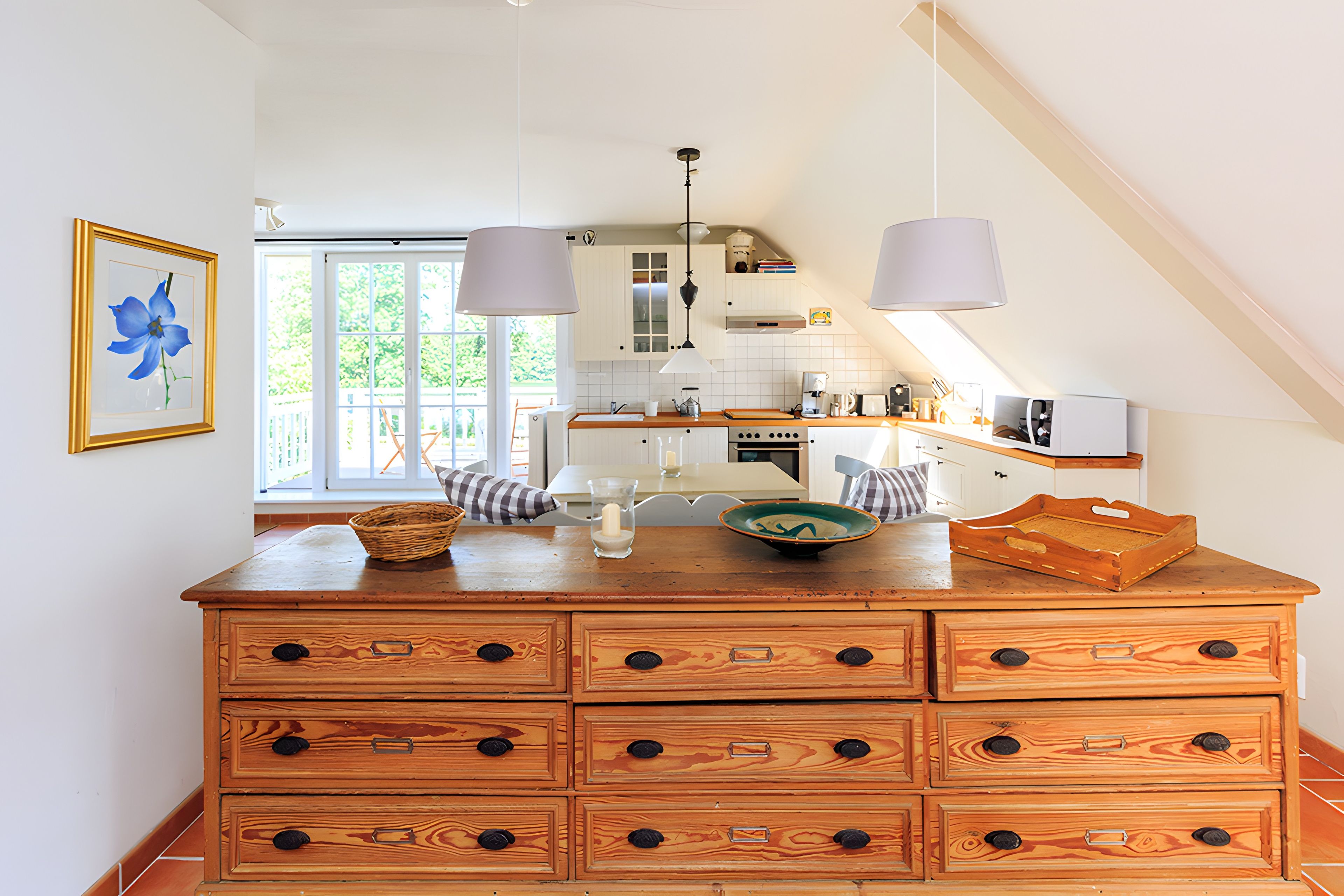A kitchen with a wooden chest of drawers, a window, and a hanging light fixture.