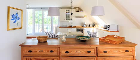 A kitchen with a wooden chest of drawers, a window, and a hanging light fixture.